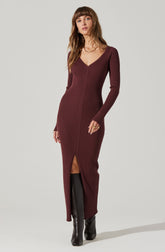A woman is wearing a long, fitted, ribbed knit dress in a deep burgundy color. The dress features a V-neckline, long sleeves, and a front slit that reaches just above the knee. She has paired the dress with black knee-high boots.